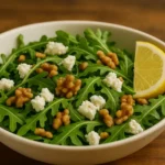 Arugula goat cheese salad with lemon vinaigrette and toasted walnuts in a white bowl.