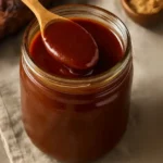 Jar of thick Kansas-style BBQ sauce with a deep reddish-brown color on a wooden table.