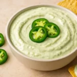 A bowl of creamy jalapeño cream cheese dip garnished with sliced jalapeños and served with tortilla chips.